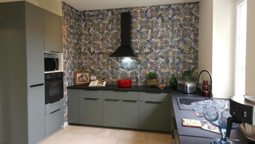 a kitchen with gray cabinets and a patterned wall at Maison d'hôtes Café Bulle in Jonquery
