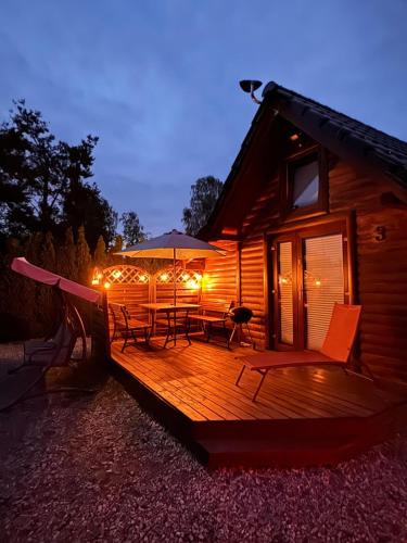 a wooden deck with chairs and an umbrella on a cabin at Karmelowe Domki Kaszuby, z jacuzzi na tarasie z widokiem na jezioro in Stężyca