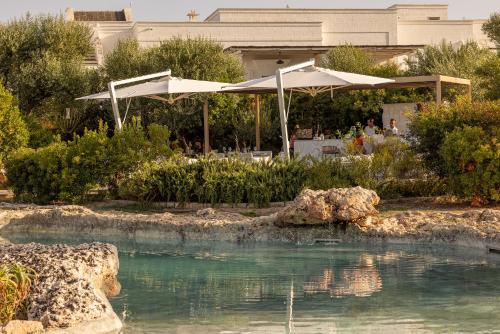a pool of water with two umbrellas in a garden at Masseria San Francesco in Savelletri di Fasano