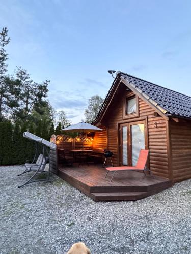 a cabin with a deck with a table and chairs at Karmelowe Domki Kaszuby, z jacuzzi na tarasie z widokiem na jezioro in Stężyca