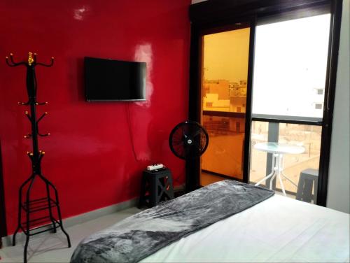 een slaapkamer met een rode muur met een bed en een flatscreen-tv bij Belle petite chambre calme à Ngor, Dakar in Dakar