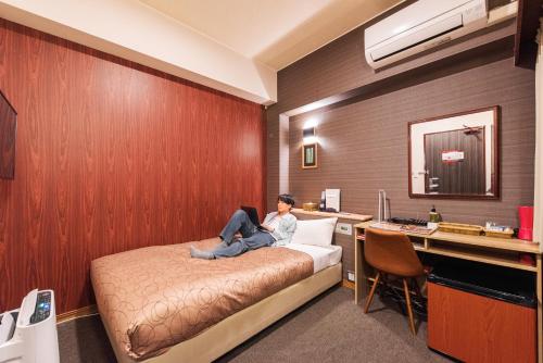 a woman sitting on a bed in a room at HOTEL RELIEF Kokura Station in Kitakyushu