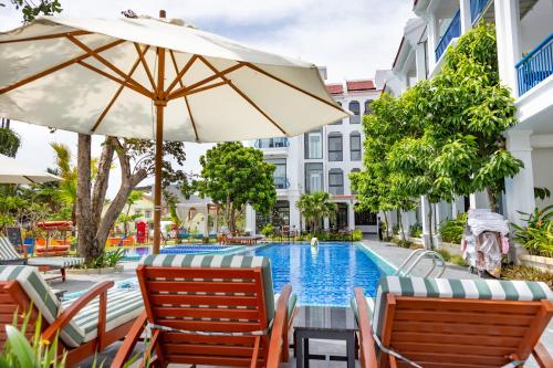 a pool with chairs and an umbrella next to a hotel at Serene Nature Hotel & Spa in Hoi An