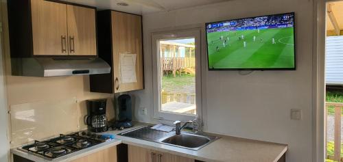 Il comprend une cuisine avec un évier et une télévision murale. dans l'établissement Mobil Home S24 - Camping Phare d'Opale, à Le Portel