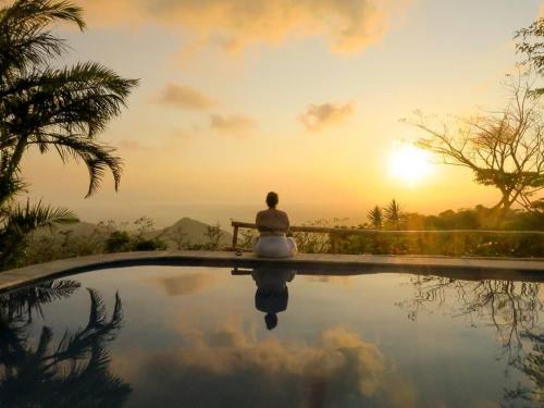 a person sitting on a bench by a pool with the sunset at Lodge Mirador - Great Swimming pool - Kitchen - BBQ - Netflix in Tajo Alto
