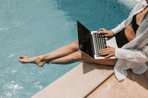 a woman sitting next to a swimming pool with a laptop at Naxian Air in Agios Georgios