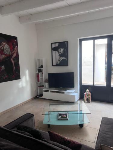 - un salon avec une télévision et une table basse en verre dans l'établissement La Maison Perrin, à Aigues-Mortes