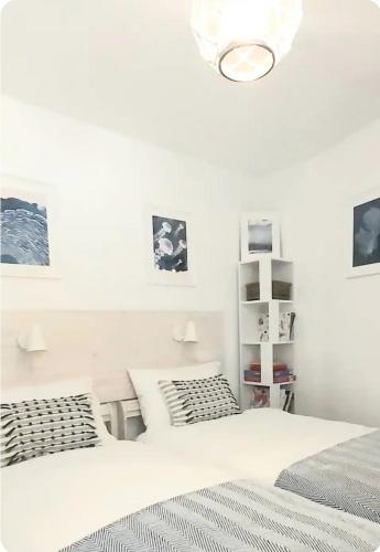 a white bedroom with two beds and a chandelier at Kindly Light Beach House, Borth-y-Gest in Porthmadog