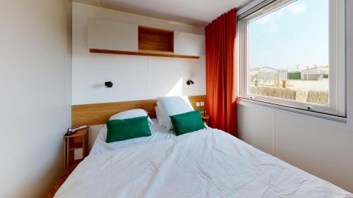 une chambre avec un lit avec des oreillers verts et une fenêtre dans l'établissement Mobil Home avec Clim La Plage, à La Parée Preneau
