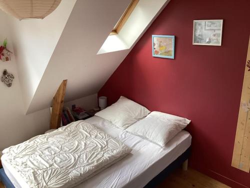 Ce lit se trouve dans une chambre dotée d'un mur rouge. dans l'établissement Jolie Maison proche plage Sables Blancs, à Concarneau