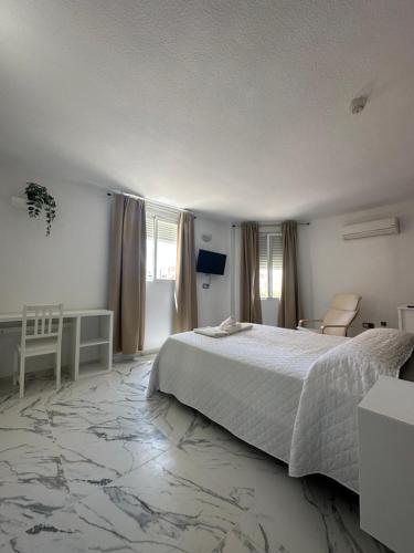 a white bedroom with a bed and a chair at Hotel Avenida in Vélez-Málaga