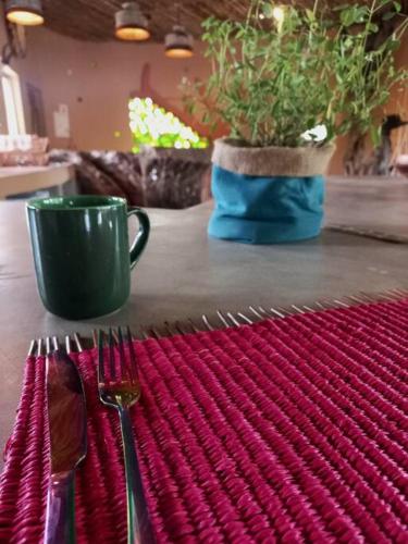 a table with a fork and a cup and a potted plant at The Eco Hut in Hoedspruit