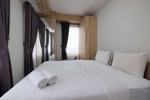 a bedroom with a white bed with two towels on it at Modern Look and Comfy 2BR Transpark Cibubur Apartment By Travelio in Depok