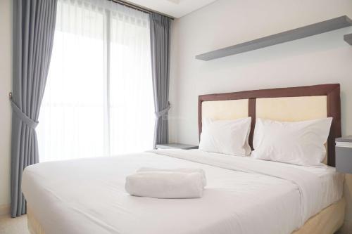 a white bed with a white pillow on top of it at Minimalist and Nice Studio at Gold Coast Apartment By Travelio in Jakarta