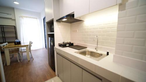a white kitchen with a sink and a table at Wonderful 2BR Combine at Bale Hinggil Apartment By Travelio in Medokanayu
