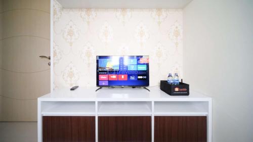a tv on a white stand with a desk at Best Choice and Cozy Living 2BR at Bale Hinggil Apartment By Travelio in Medokanayu