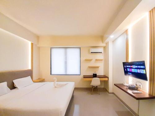 SeturanにあるBest Homey and Restful Studio at Altuz Seturan Yogyakarta Apartment By Travelioのベッドと机とテレビのある寝室