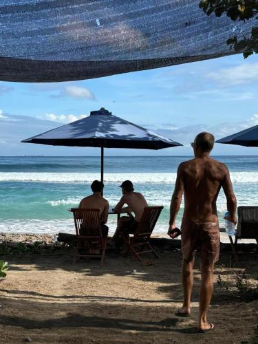 three men sitting in chairs under an umbrella on the beach at Dessert Point Bungalow in Sekotong