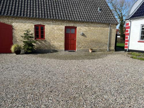 a brick house with red doors and a gravel driveway at Ferielejlighed in Nørre Åby