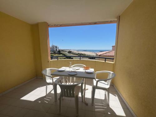 une table et des chaises sur un balcon avec une grande fenêtre dans l'établissement SAVANNA BEACH I Agréable T2 avec belle vue mer piscine Rochelongue Cap d'Agde, au Cap d'Agde
