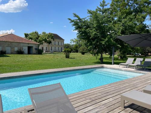 une piscine avec deux chaises et un parasol dans l'établissement Demeure de charme proche Saint-Emilion - Piscine et Parc, à Flaujagues