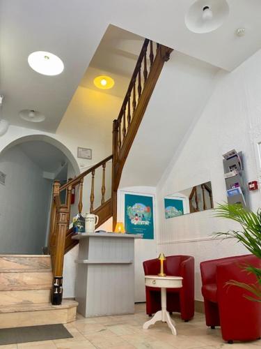 a lobby with a staircase and red chairs and a table at Hôtel De Normandie in Amiens