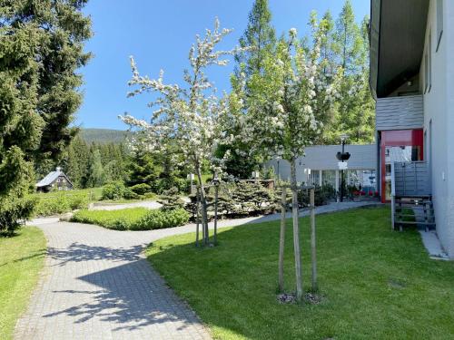 a garden with trees in the grass next to a building at Apartmán Resident A001 - BEZBARIÉROVÝ Apartmán ideální pro rodiny s dětmi, v těsné blízkosti Anenského údolí, bobové dráhy, Ski areálů, Ski školy, FREE PARKING, FREE WIFI, výhled do zahrady s posezením na terase, dětské hřiště v areálu in Harrachov