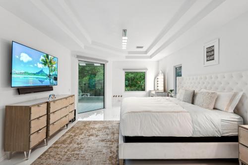 a white bedroom with a large bed and a flat screen tv at Luxury Modern Waterfront House in BEST Location! King Bed Suite & Close to Beach in West Palm Beach