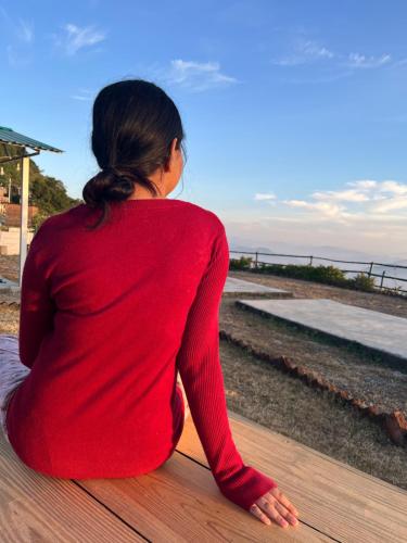 a woman sitting on a wooden floor looking at the ocean at Kunjapuri camps & Cottage in Narendranagar