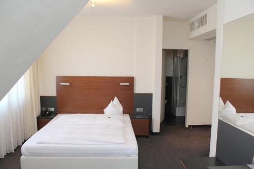 Hotel am Hirschgarten في فيلدرشتادت: غرفة نوم مع سرير أبيض كبير مع اللوح الأمامي الخشبي