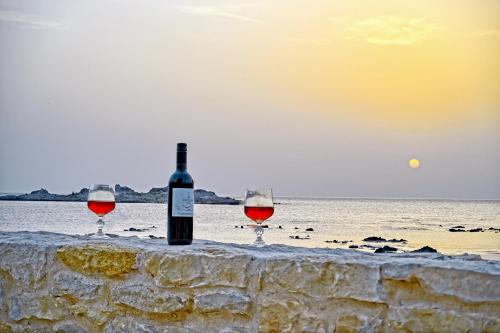 two glasses of wine sitting on a wall next to the ocean at Baloma Studio in Áyios Fótios