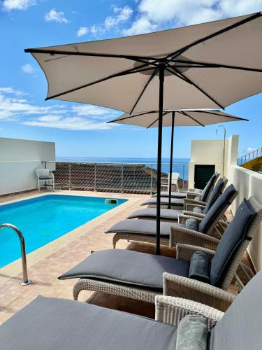 a group of chairs with an umbrella next to a swimming pool at Boutique Hotel Jardim Do Mar in Jardim do Mar