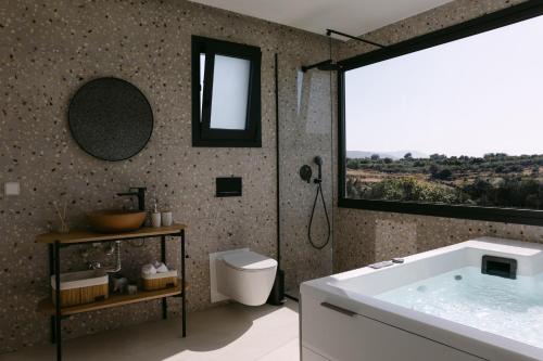 a bathroom with a tub and a toilet and a window at Emerald Harmony Villa with Private Pool & Jacuzzi in Skouloúfia