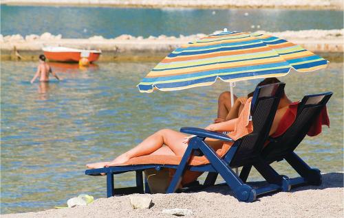two people sitting in chairs under an umbrella on a beach at 1 Bedroom Nice Apartment In Rovanjska in Rovanjska