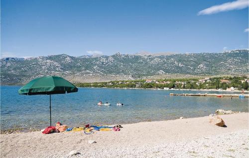 a green umbrella on a beach with people in the water at 1 Bedroom Nice Apartment In Rovanjska in Rovanjska