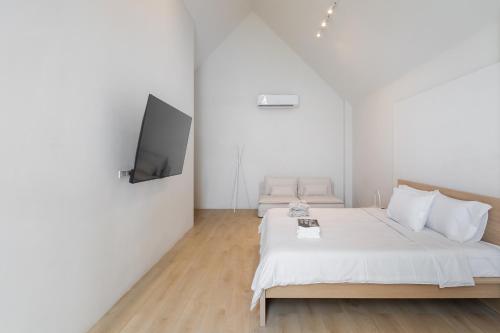a white bedroom with a bed and a flat screen tv at Nidhra นิทรา in Ban Lat Krachaeng
