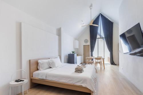 a white bedroom with a bed and a table at Nidhra นิทรา in Ban Lat Krachaeng