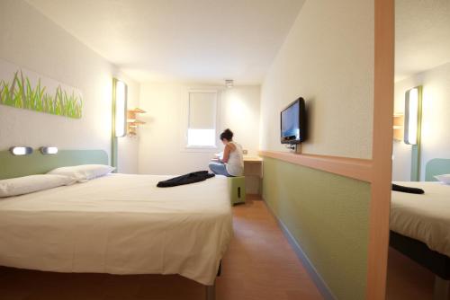 a woman sitting in a hotel room with two beds at ibis budget Saint Paul Les Dax in Saint-Paul-lès-Dax