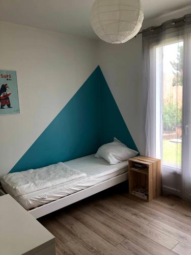 Ce lit se trouve dans un dortoir doté d'un mur bleu et d'une fenêtre. dans l'établissement Charmante Maison Entre Lac et Océan, à La Teste-de-Buch
