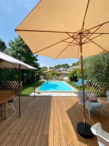 un grand parasol sur une terrasse en bois avec une piscine dans l'établissement Villa avec piscine au bassin d'Arcachon, à Gujan-Mestras