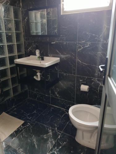 e bagno piastrellato nero con servizi igienici e lavandino. di Elite Serviços Lda a Chibungo