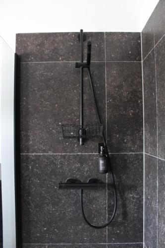 a shower in a bathroom with a black tile wall at koetshuis in Ypres