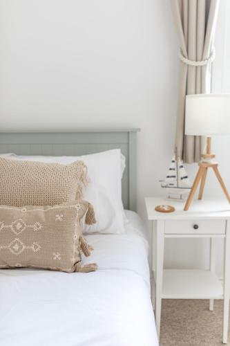 a white bedroom with a bed and a nightstand with a lamp at Charming Beachside Town House in Ryde