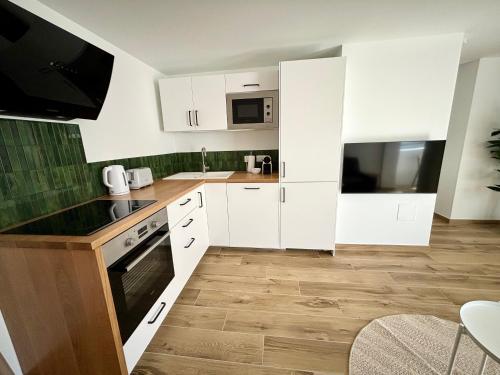 une petite cuisine avec des placards blancs et une télévision dans l'établissement Centre Ville & Plage à 200m - Clim - Parking Privé - Netflix, au Grau-du-Roi