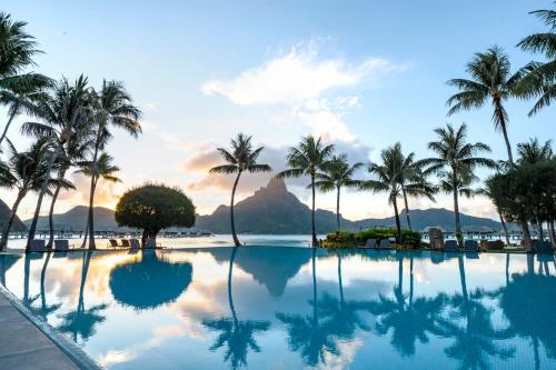 a pool with palm trees and a mountain in the background at InterContinental Bora Bora & Thalasso Spa by IHG in Bora Bora