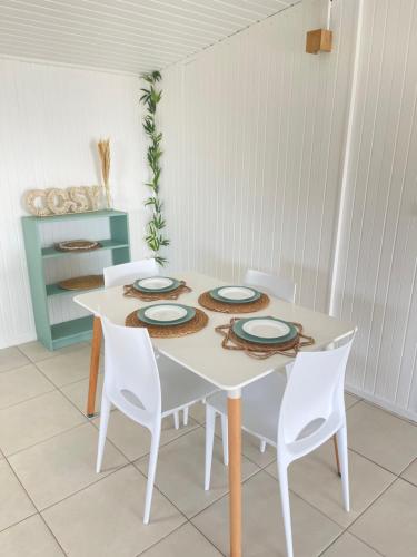 a table with white chairs and a white table with plates on it at Appartement Les Balisiers - T3 spacieux vue sur mer in Trois-Rivières