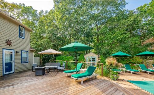 a wooden deck with green chairs and umbrellas at Villa Baloch- w/ Sparkling heated pool in East Hampton