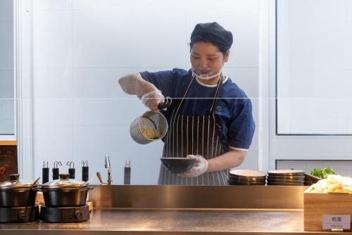 a man in a kitchen cooking food in a bowl at Atour Light Hotel Shanghai Daning International Shibei High-tech Park in Shanghai