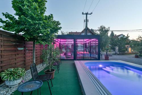 a swimming pool with chairs and a house with pink lights at Helka Apartmanház in Balatonlelle