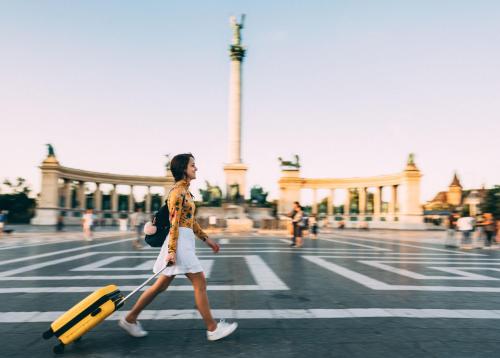 a woman walking down a street with a yellow suitcase at Verdi Budapest Aquincum in Budapest